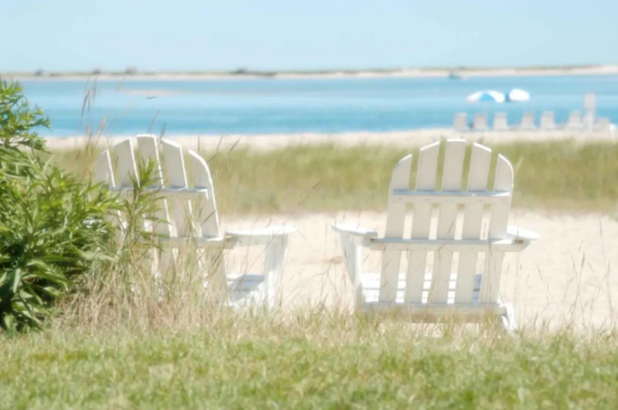 Two white adirondack chairs on cape cod beach
